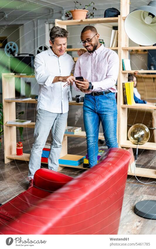 Two smiling businessmen using cell phone in loft office lofts smile mobile phone mobiles mobile phones Cellphone cell phones Businessman Business man