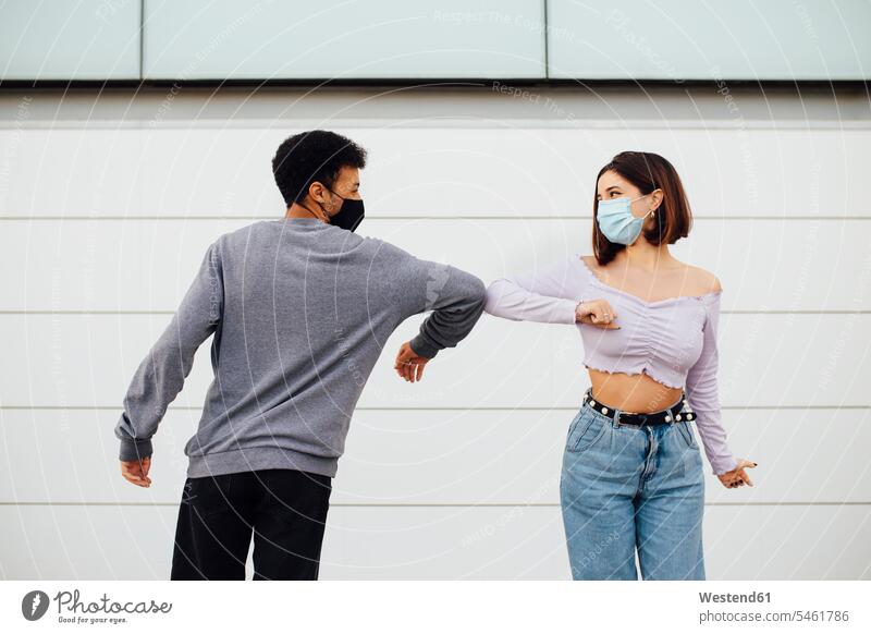 Young couple wearing face mask greeting with elbow bump while standing against wall color image colour image outdoors location shots outdoor shot outdoor shots