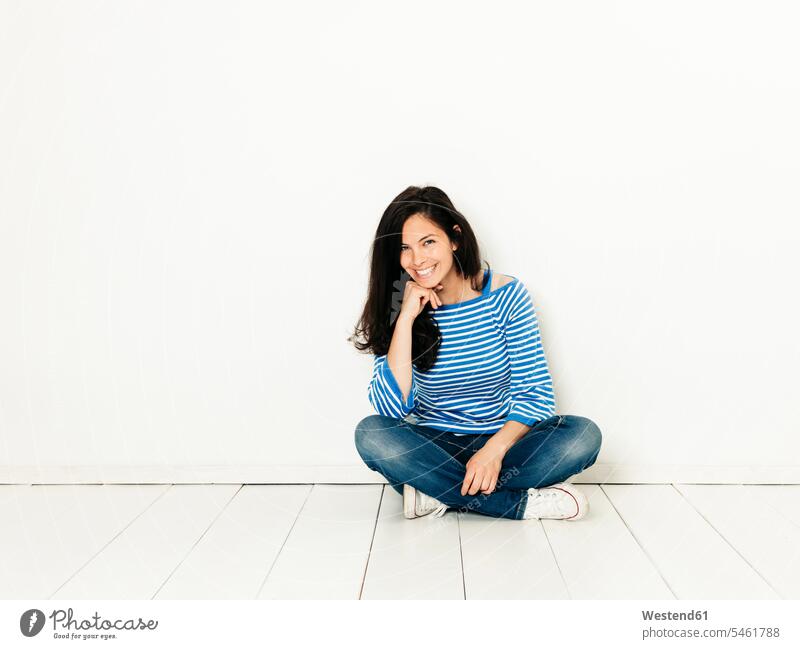 Beautiful young woman with black hair and blue white striped sweater sitting on the ground in front of white background caucasian caucasian ethnicity