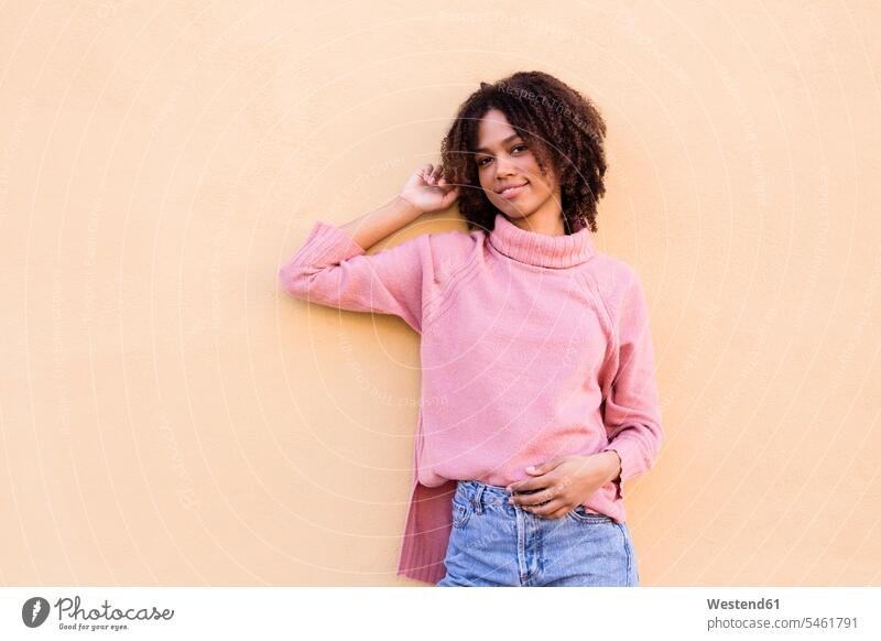 Portrait of smiling young woman wearing pink turtleneck pullover leaning against wall Rosy walls smile females women portrait portraits sweater jumper Sweaters
