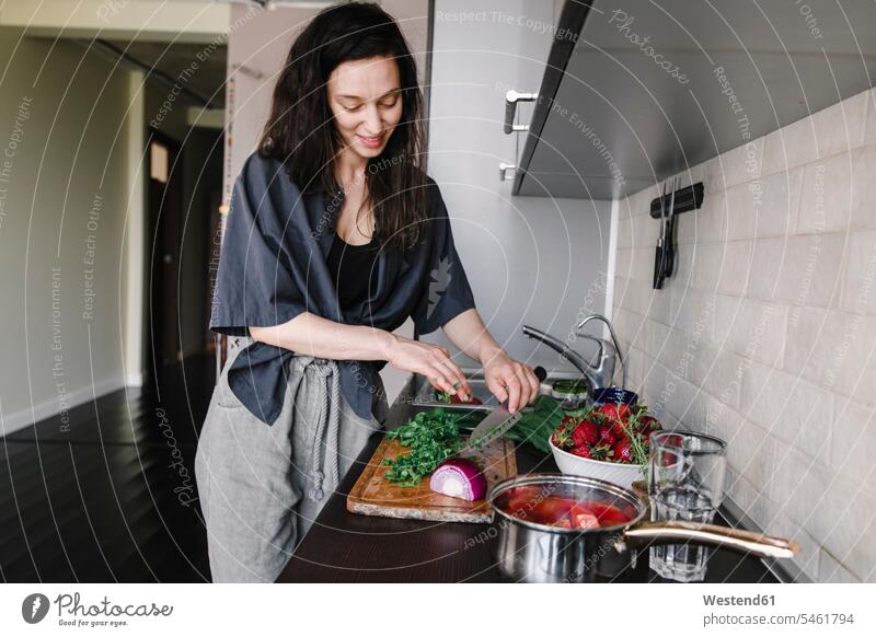 Smiling woman preparing salad in the kitchen Crockery Tableware Bowls cook smile cut delight enjoyment Pleasant pleasure pleased stand at home free time