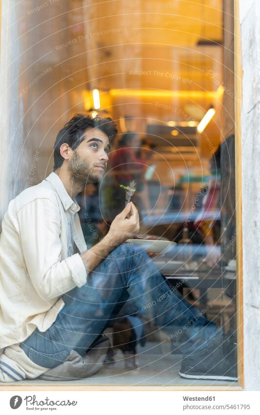 Man eating a salad sitting at the window in a restaurant looking out human human being human beings humans person persons celibate celibates singles
