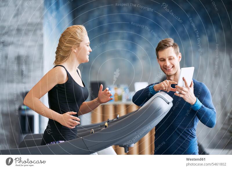 Woman running on treadmill with personal trainer at gym woman females women gyms Health Club coach coaches Treadmills running machine Adults grown-ups grownups