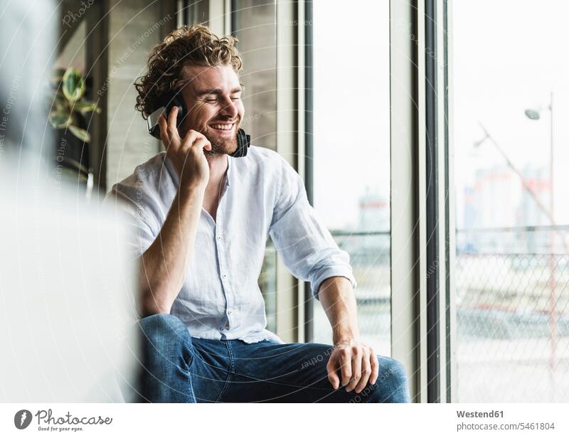 Happy casual young man listening to music with headphones at the window happiness happy windows men males hearing headset Adults grown-ups grownups adult people