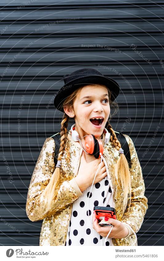 Portrait of astonished girl with headphones and smartphone wearing hat and golden sequin jacket puzzled wonder wondering sequins Smartphone iPhone Smartphones