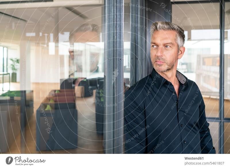 Buinessman standing in office, leaning on glass wall, thinking human human being human beings humans person persons caucasian appearance caucasian ethnicity