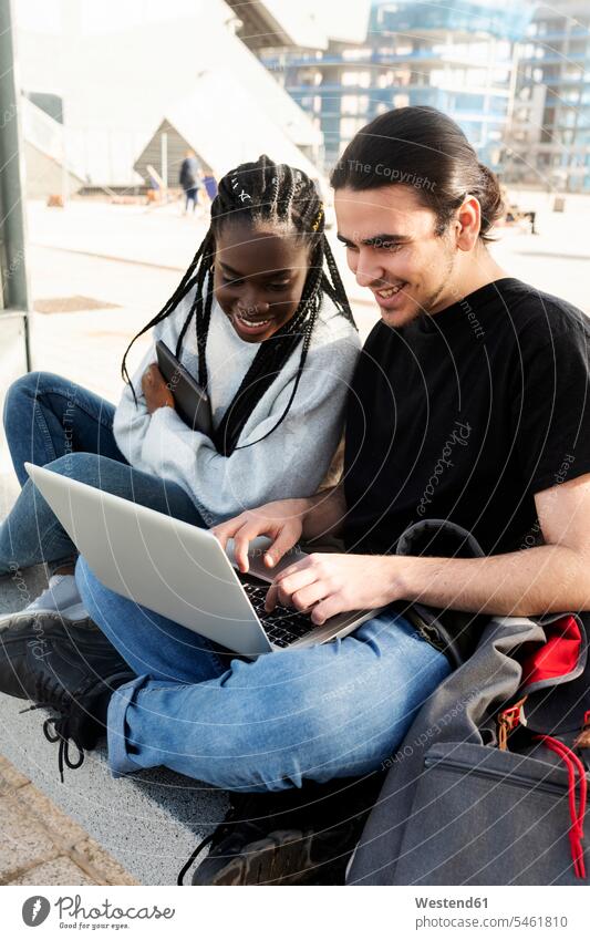 Happy young couple using laptop at tram stop friends mate back-pack back-packs backpacks rucksack rucksacks pants Trouser Denim Jeans benches computers