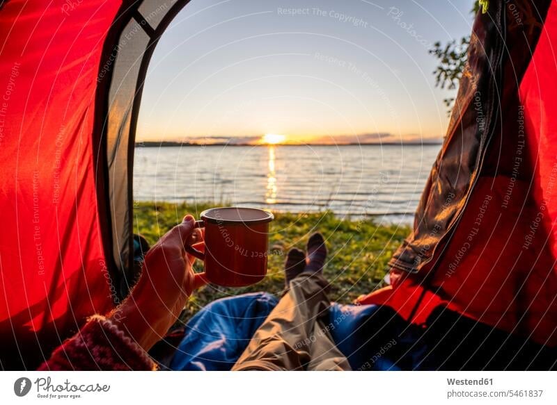 Man camping in Estonia, watching sunset lying in tent lake lakes open opened leg legs human leg human legs drinking resting cup tents nature natural world Cup