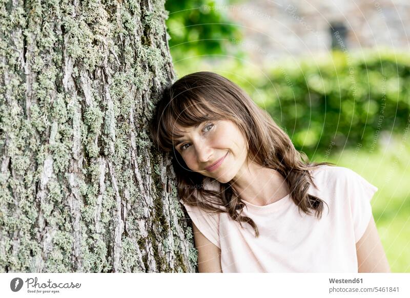 Portrait of smiling brunette woman leaning against a tree trunk human human being human beings humans person persons caucasian appearance caucasian ethnicity