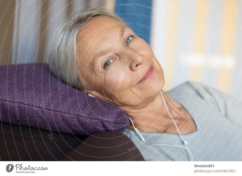 Portrait of smiling senior woman lying on the couch at home listening music with earphones females women senior women elder women elder woman old laying down