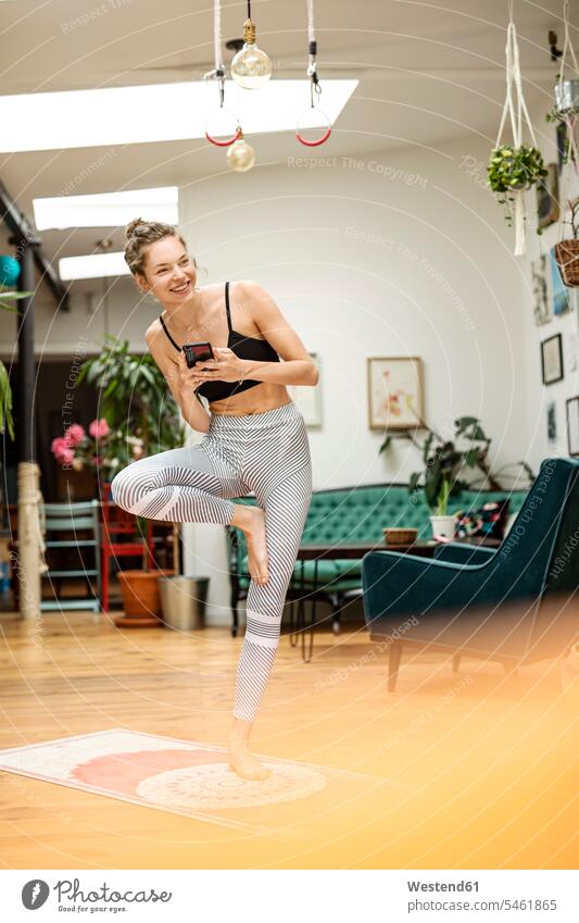 Young woman practicing yoga at home, holding smartphone chairs Arm Chair Arm Chairs armchairs telecommunication phones telephone telephones cell phone