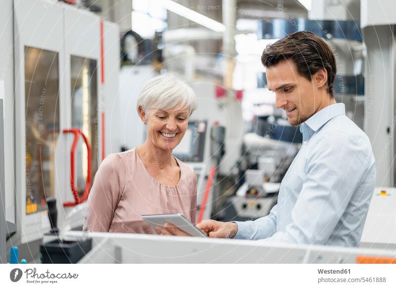 Smiling businessman and senior woman with tablet talking in a factory speaking smiling smile factories females women Businessman Business man Businessmen