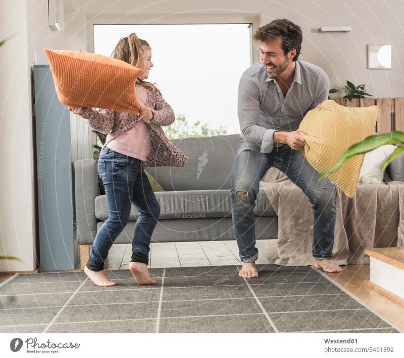 Young man and little girl having a pillow fight in the living room hitting beating family with one child living rooms livingroom single parent one parent