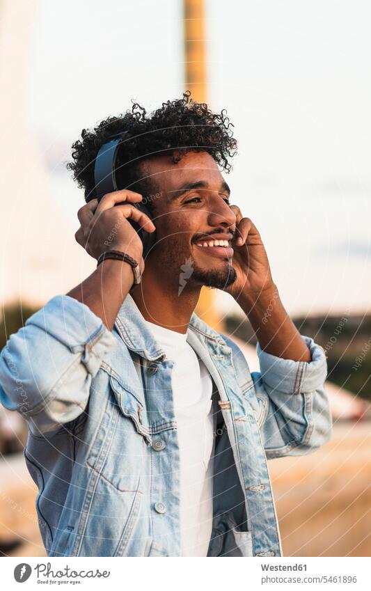 Close-up of smiling young man listening music through headphones against clear sky color image colour image Spain leisure activity leisure activities free time