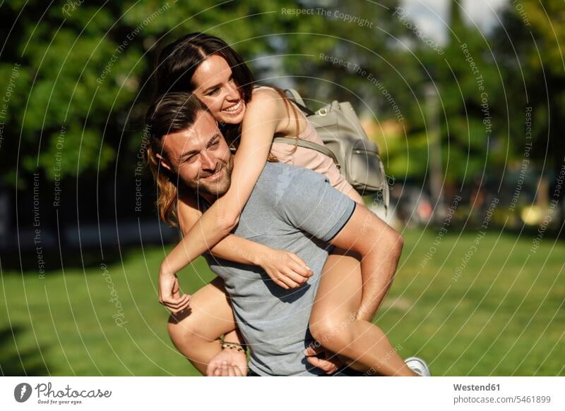 Happy man giving girlfriend a piggyback ride in park parks happiness happy carrying piggy-back pickaback Piggybacking Piggy Back couple twosomes partnership