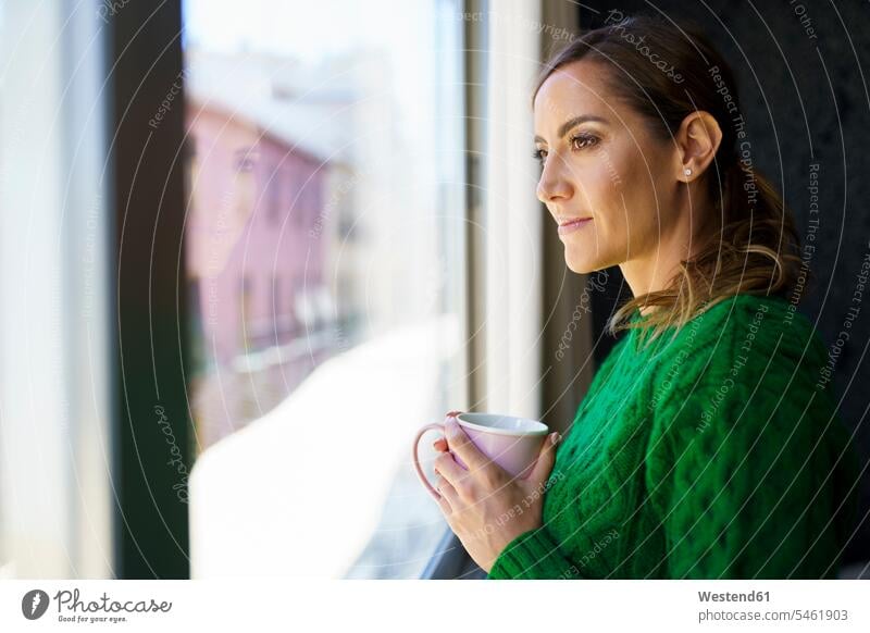 Woman holding coffee cup while standing by window at home color image colour image indoors indoor shot indoor shots interior interior view Interiors day