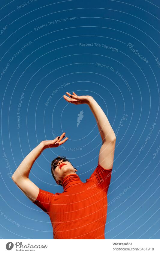 Non-binary male with hand raised standing against clear sky on sunny day color image colour image outdoors location shots outdoor shot outdoor shots