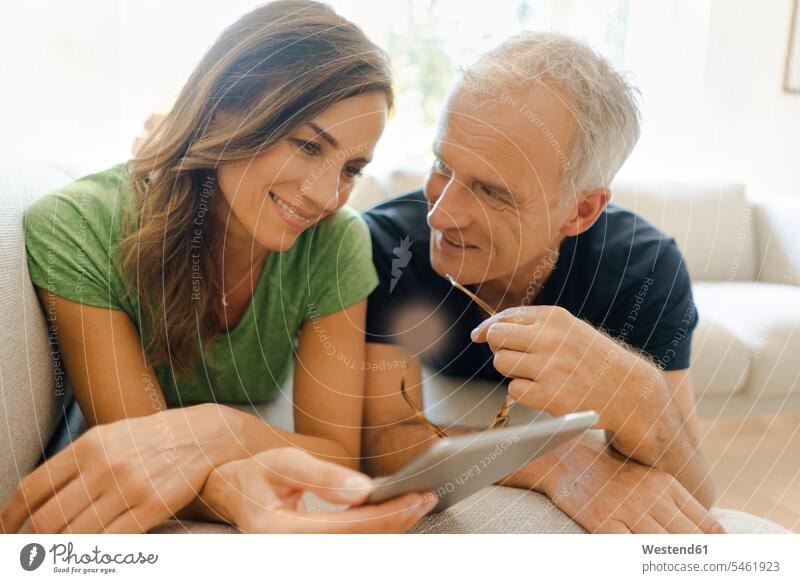 Smiling mature couple lying on couch at home sharing tablet couches settee settees sofa sofas laying down lie lying down share smile computers Digital Tablet