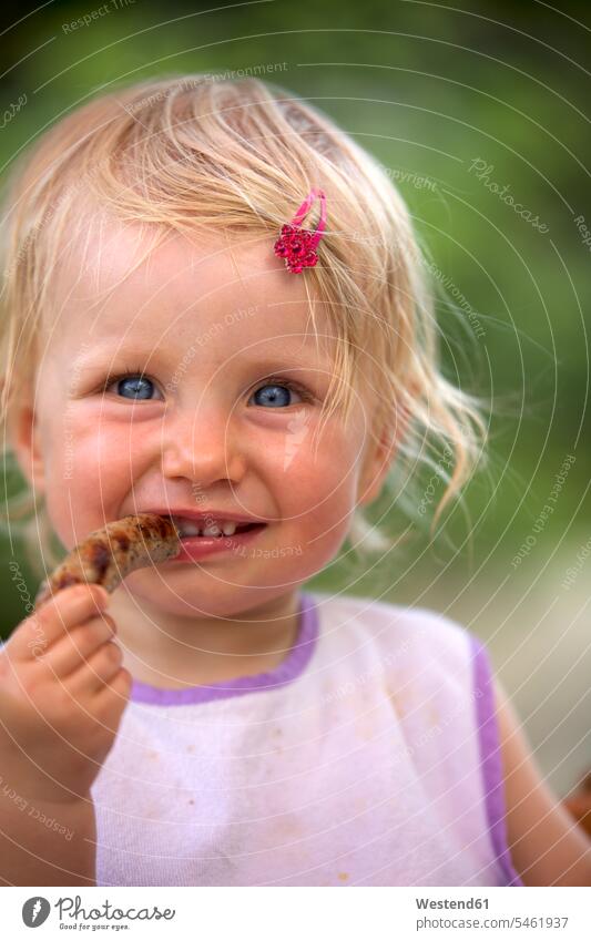 Portrait of blond little girl with bib and pink haipin eating sausage smiling smile childhood Sausage Sausages bibs Baby Bib hairpin hairpins nature
