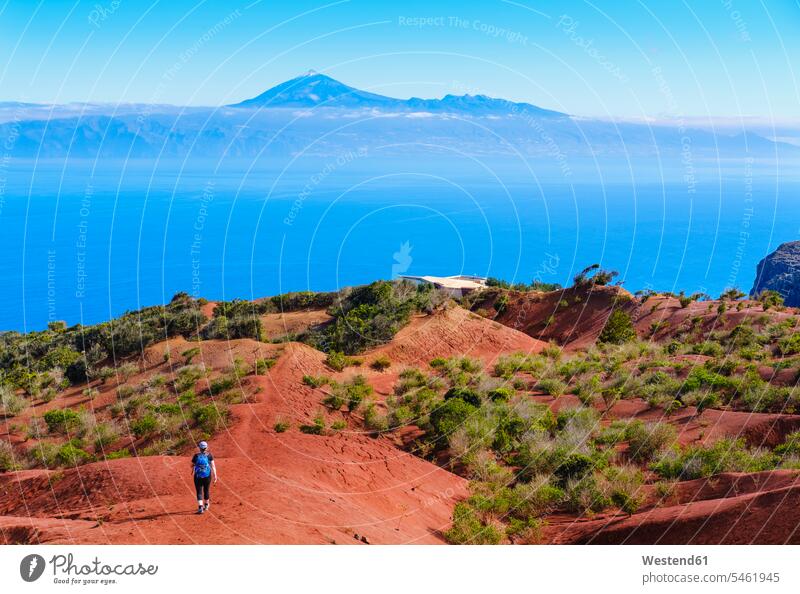 Spain, Canary Islands, Agulo, Female backpacker hiking toward Mirador de Abrante observation point with Mount Teide in distant background outdoors