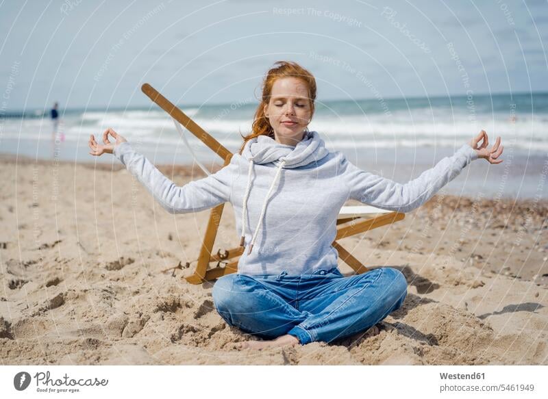 Woman sitting cross-legged on sand, meditating on the beach deckchair deck chair deckchairs deck chairs woman females women beaches yoga meditation meditations