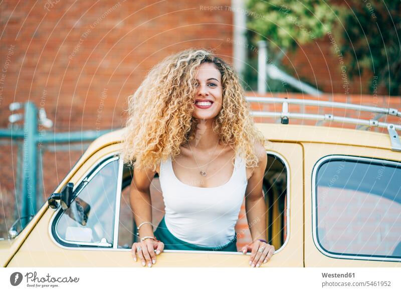Portrait of happy blond woman leaning out of window of classic car females women vintage car happiness blond hair blonde hair car window car windows portrait