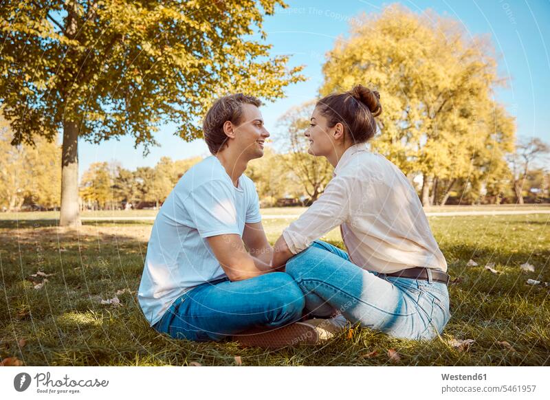 Young couple sitting on meadow at a park meadows parks Seated twosomes partnership couples people persons human being humans human beings opposite togetherness
