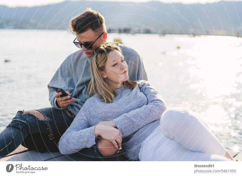 Young couple relaxing on jetty at Lake Zurich, Zurich, Switzerland telecommunication phones telephone telephones cell phone cell phones Cellphone mobile