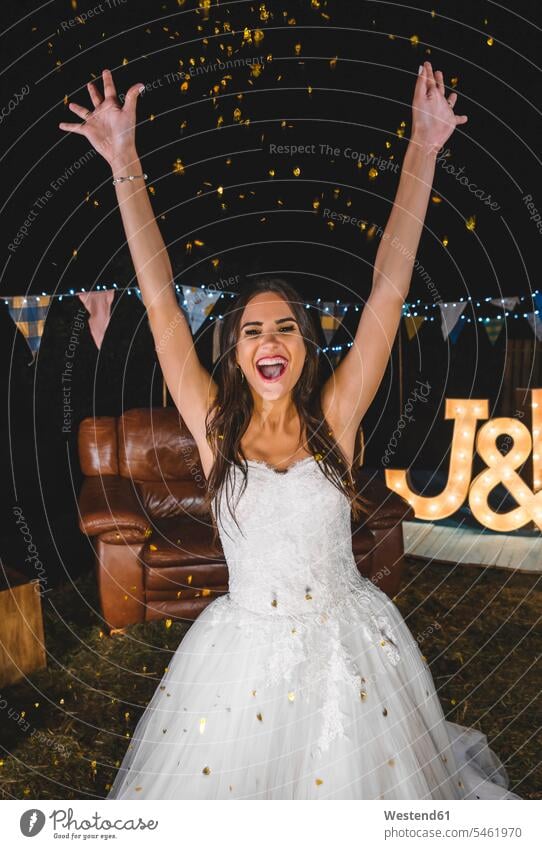 Cheerful bride raising her arms while confetti falling over her on a night party outdoors brides Wedding getting married marrying Marriage Party Parties Fun
