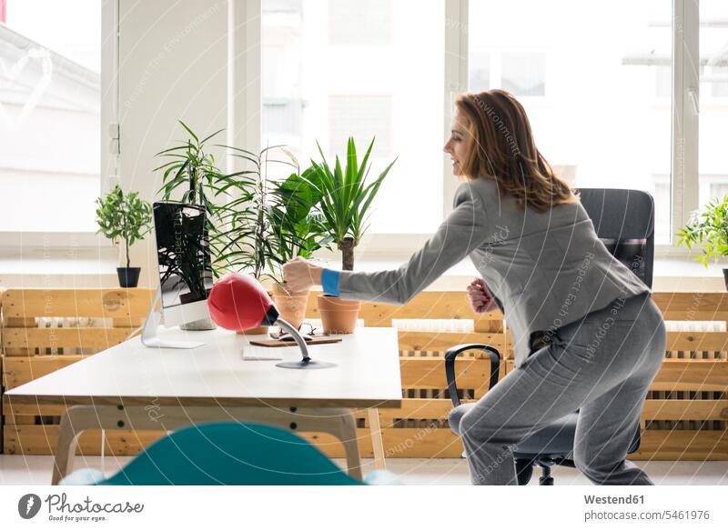 Businesswoman boxing a punchingball in her office punch ball offices office room office rooms fighting standing desk desks businesswoman businesswomen
