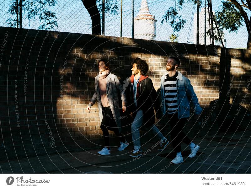 Three happy friends walking along a brick wall in shadow happiness going brick walls shadows Shades friendship fashionable togetherness style stylish Barcelona