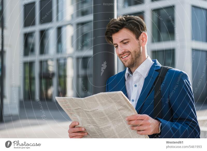 Smiling businessman reading newspaper in the city smiling smile town cities towns newspapers Businessman Business man Businessmen Business men outdoors