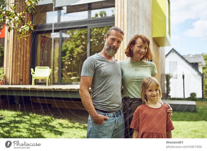 Smiling family posing while standing against tiny house in yard color image colour image Germany leisure activity leisure activities free time leisure time