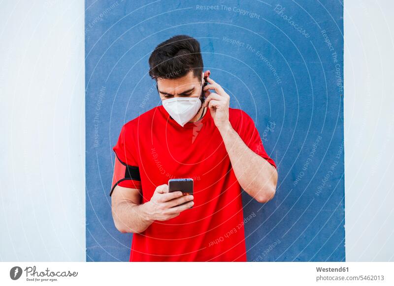 Mid adult man wearing mask using smart phone while standing against wall color image colour image Spain outdoors location shots outdoor shot outdoor shots day