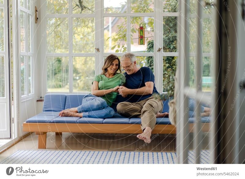 Affectionate mature couple sitting on couch at home couches settee settees sofa sofas Seated human human being human beings humans person persons couples