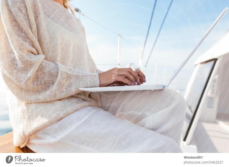 Woman sitting on catamaran, using laptop sailing trip yachting sailing trips woman females women Laptop Computers laptops notebook using a laptop Using Laptops