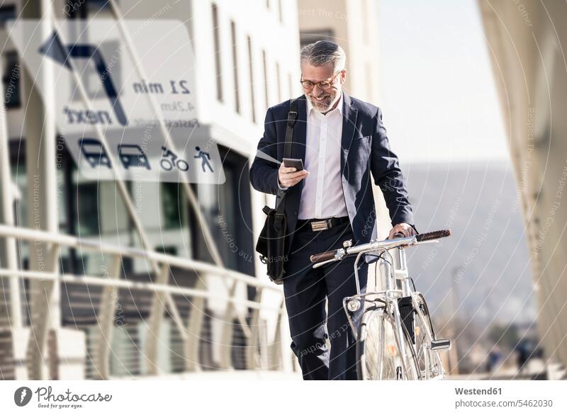 Smiling mature businessman with bicycle using cell phone for navigation in the city human human being human beings humans person persons caucasian appearance