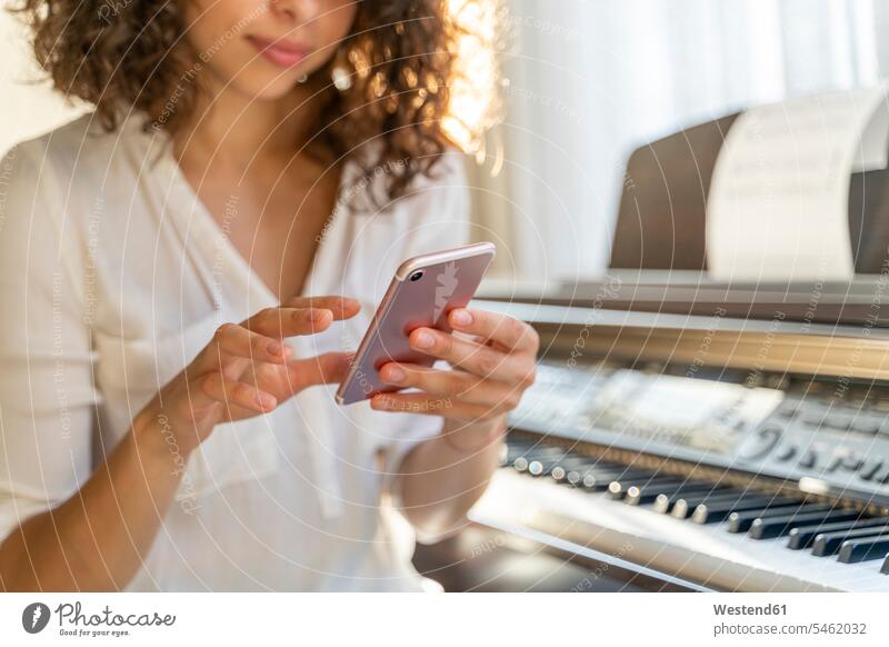 Young woman using cell phone at the piano at home human human being human beings humans person persons caucasian appearance caucasian ethnicity european 1