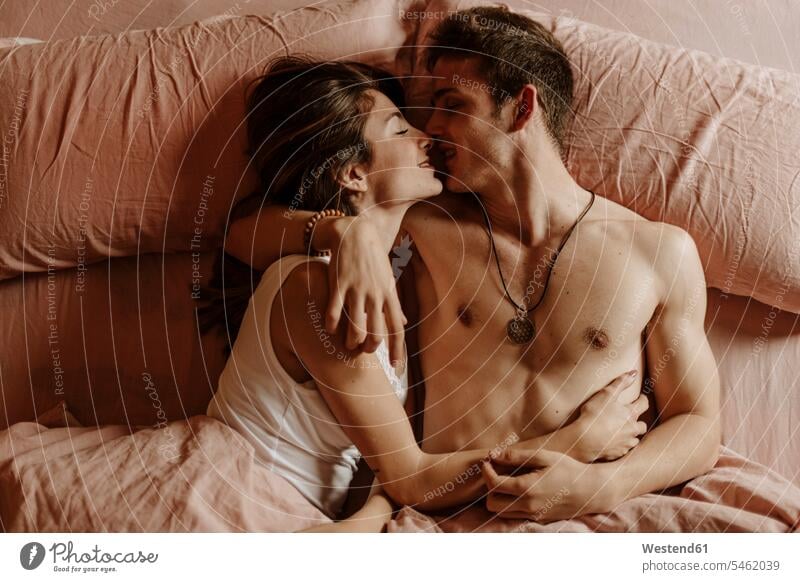 Intimate young couple lying in bed Bed - Furniture beds jewelry necklaces touch cuddle snuggle snuggling kiss kisses smile embrace Embracement hug hugging