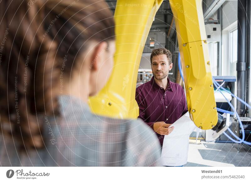 Businessman and woman having a meeting in front of industrial robots in a high tech company discussion firm checking Test testing Check high-tech maintenance