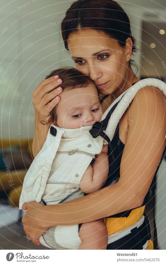 Mother carrying her baby girl in sling at home daughter daughters baby sling slings baby slings infants nurselings babies mother mommy mothers ma mummy mama
