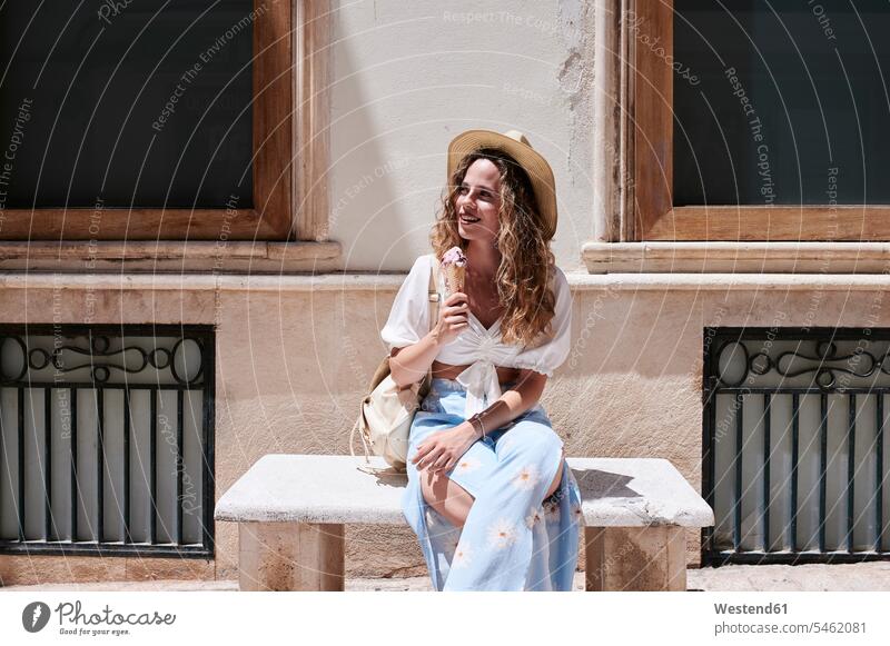 Young woman sitting on stone bench eating ice cream touristic tourists human human being human beings humans person persons curl curled curls curly hair hats