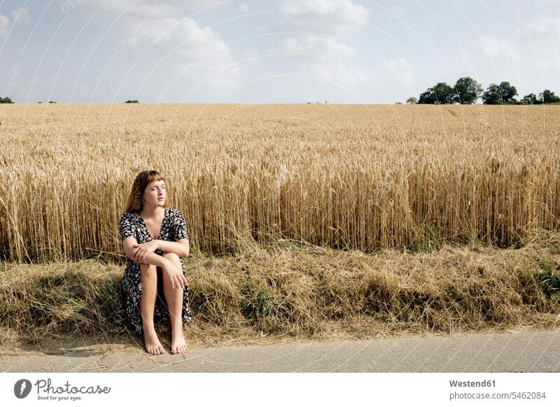 Young woman sitting barefoot at roadside in front of grain field human human being human beings humans person persons caucasian appearance caucasian ethnicity