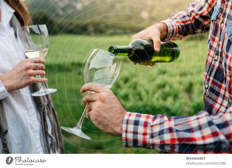 Man serving white wine in glass while standing with woman at vineyard color image colour image outdoors location shots outdoor shot outdoor shots day