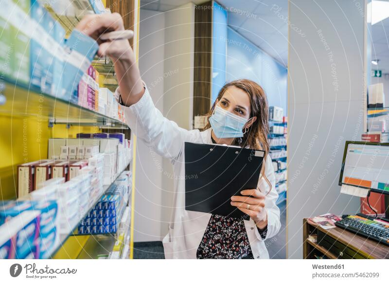 Female pharmacist wearing protective face mask while working in chemist shop color image colour image indoors indoor shot indoor shots interior interior view