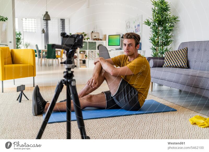 Fitness trainer recording exercise on camera while sitting on mat at home color image colour image indoors indoor shot indoor shots interior interior view