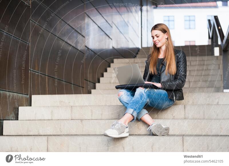 Happy young woman using laptop while sitting on steps in underground walkway color image colour image indoors indoor shot indoor shots interior interior view