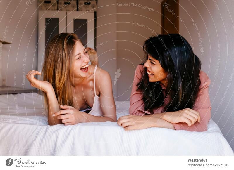 Female friends laughing while lying on bed color image colour image indoors indoor shot indoor shots interior interior view Interiors day daylight shot