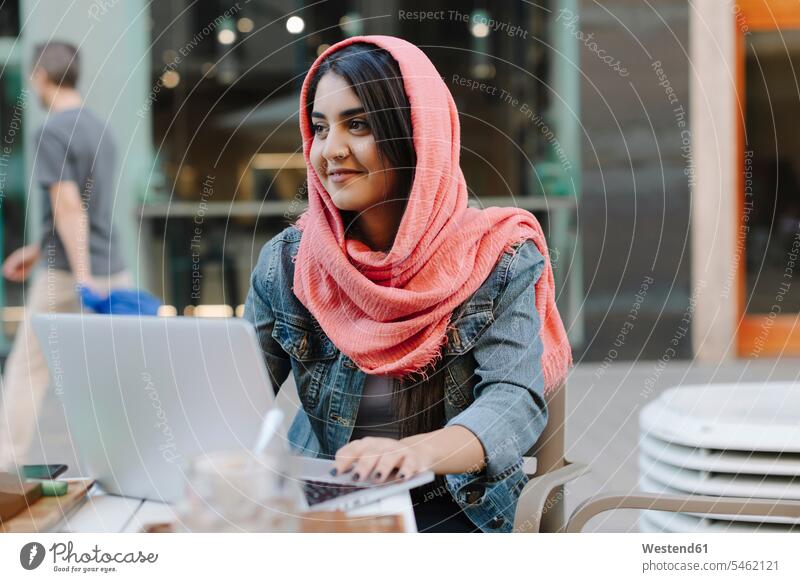 Smiling young woman with laptop wearing headscarf at a pavement cafe Internet The Internet business business world business life Wifi Wi-Fi wireless internet