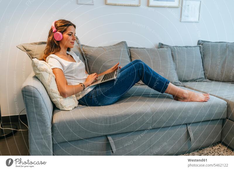 Relaxed young woman on couch at home with headphones and laptop human human being human beings humans person persons caucasian appearance caucasian ethnicity
